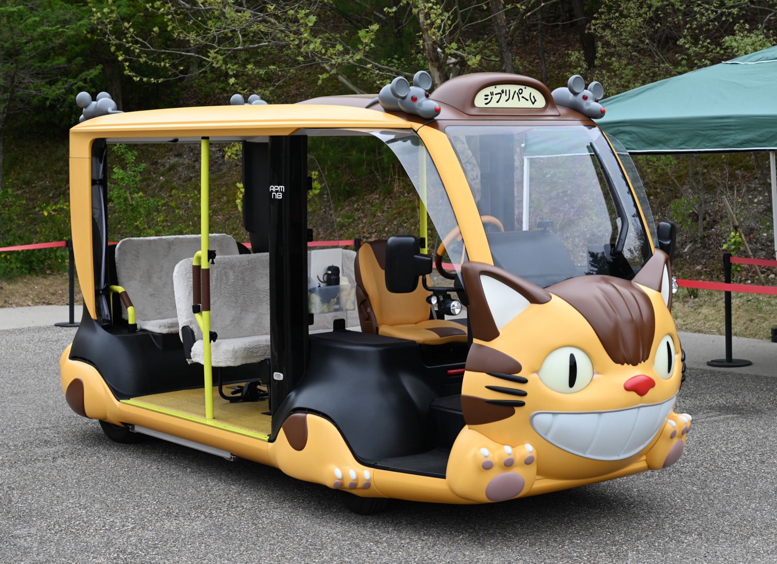吉卜力公園 龍貓巴士（ネコバス）造型電動接駁車 APM 貓巴士 — 黃色車身、貓臉車頭、車頂趴著小老鼠